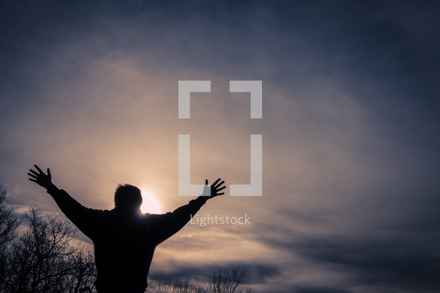 Backlit man with arms up in sunset
