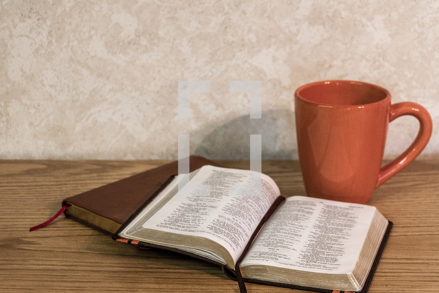 Bible open on desk with coffee cup and brown leather journal