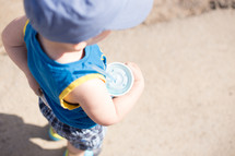 toddler boy holding a drink on a beach 