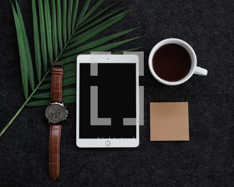 A sprig of green leaves, wristwatch, cell phone, cup of coffee and a blank notecard.