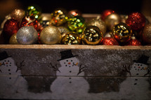 Multi-colored Christmas balls in a wooden box painted with snowmen.