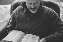A man reading a Bible sitting in a chair 