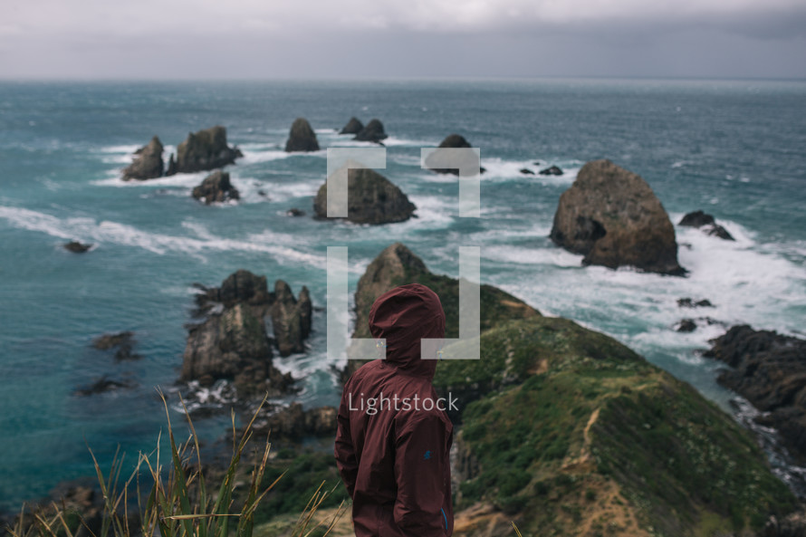 rock formations in the ocean along the shores of New Zealand and a man in a hoodie 