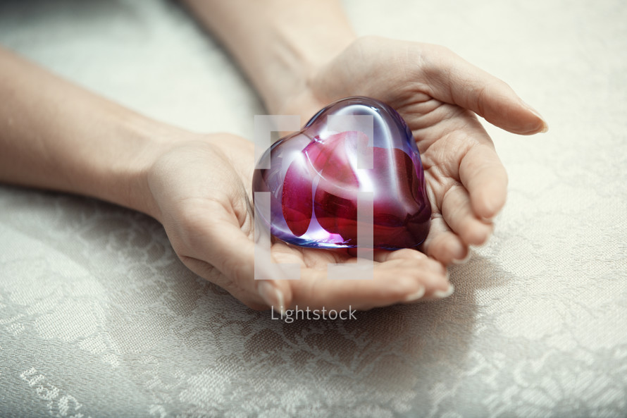 cupped hands holding a glass heart 
