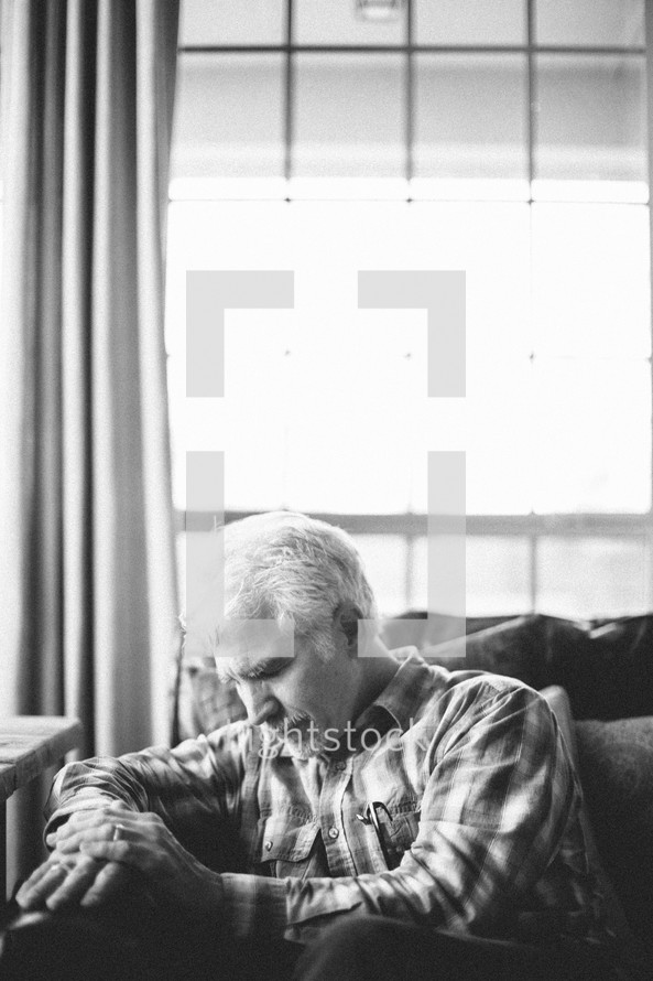 elderly man sitting on a couch with his head bowed in prayer