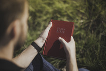 a man sitting in grass holding a Bible 