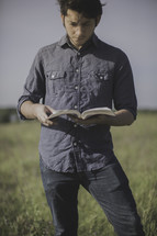 a man standing in a field of tall grass reading a Bible 