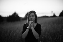 a woman standing in a field with praying hands 