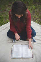 teenage girl sitting on a blanket reading a Bible 