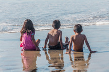 children sitting on a beach letting the tide wash over them 
