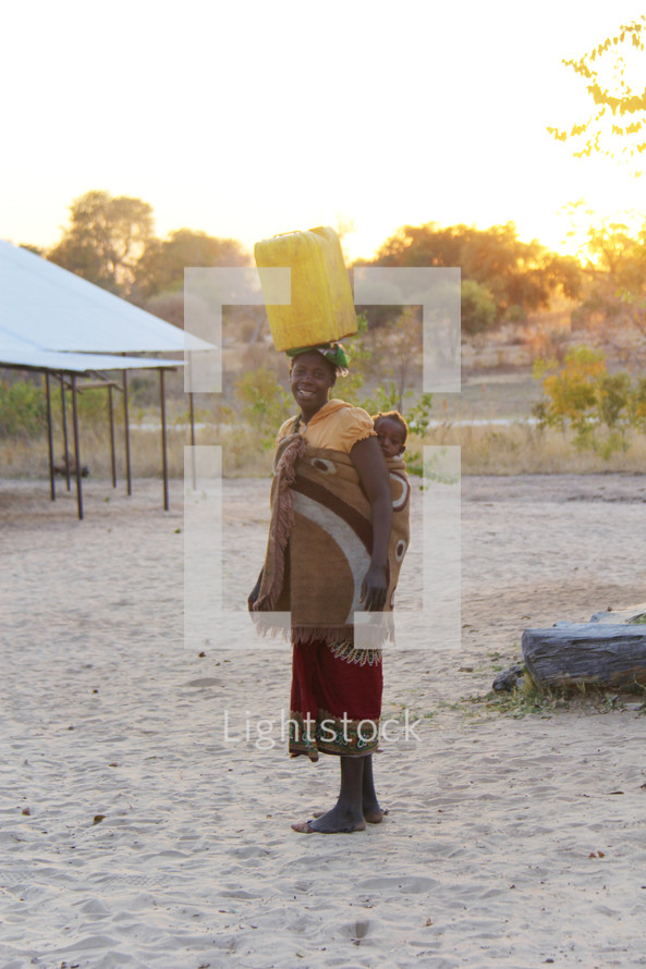 a woman with her baby carrying water on her head in a village 