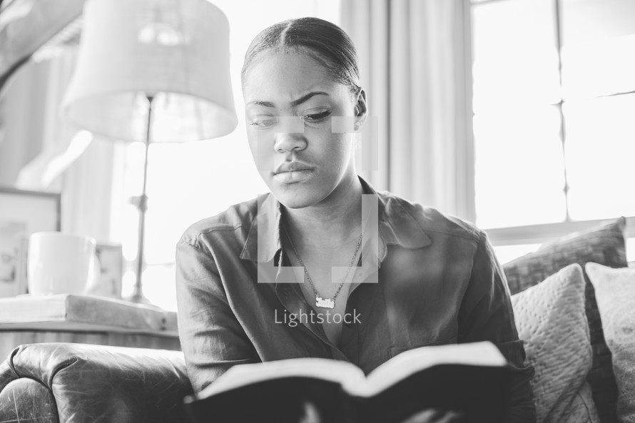 Woman reading the Bible while sitting on a sofa.