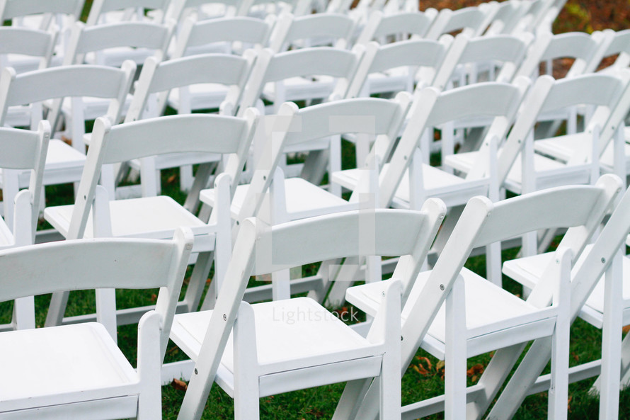 rows of white folding chairs at an outdoor wedding 