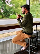 a man drinking coffee sitting in a window 