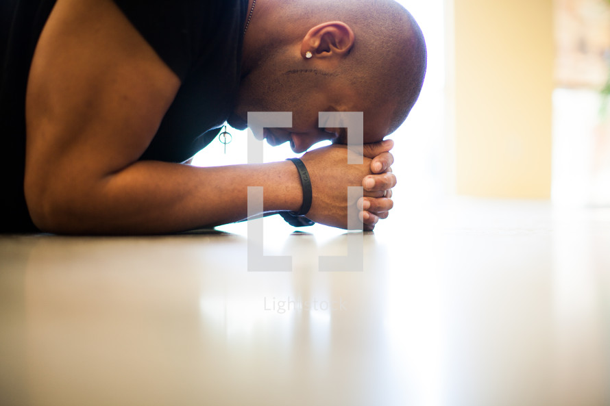Man with head on hands, praying on the floor.