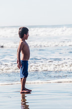 boy child standing on wet sand on a beach 