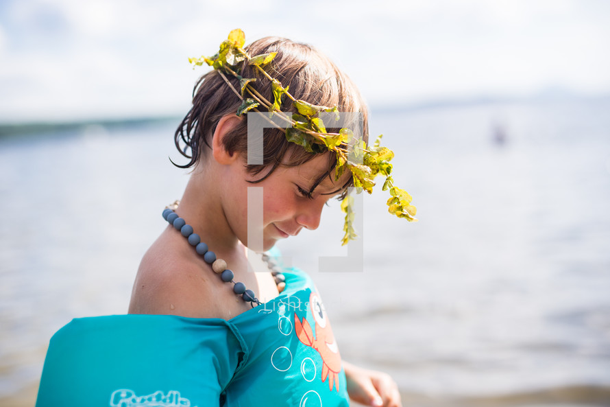 a child in a floatie playing at a lake with a crown of leaves 