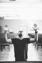 man on his knees with his hands raised in worship and praise to God in a church