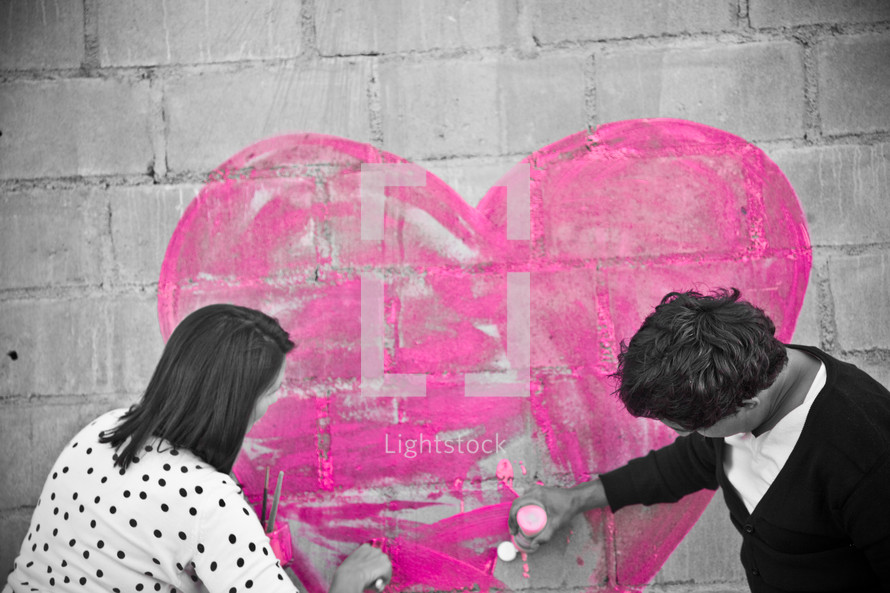 Couple painting a heart on a brick wall.