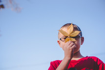 boy holding a fall leaf over his face