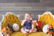 an infant sitting on a couch with stuffed animals 