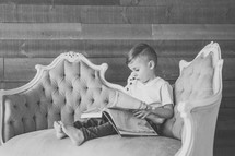 a boy child sitting on a couch reading a book 