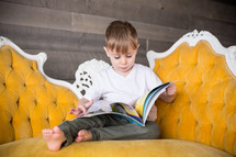 a boy child sitting on a couch reading a Book 