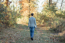 a man in a blazer carrying a Bible walking into a forest 
