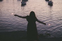 silhouette of a woman holding sparklers in front of water 