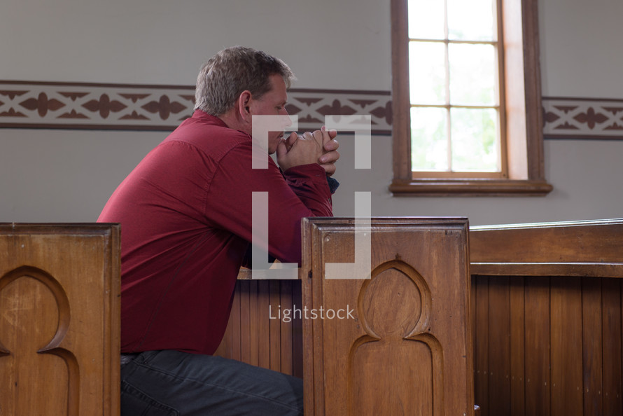 a man praying alone in church pews 