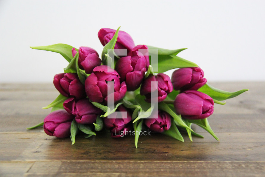  A bunch of purple tulips laying on a wooden table.
