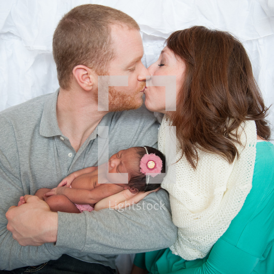 Kissing couple holding a newborn infant.