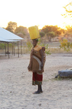 a woman with her baby carrying water on her head in a village 