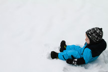 a toddler boy in a snowsuit sitting in snow 