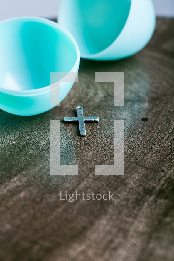 Silver cross on a wooden table with a plastic Easter egg.