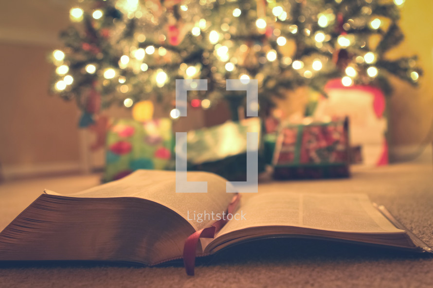 Open Bible and gifts under a Christmas tree 