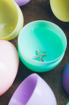 Silver cross inside a plastic Easter egg.