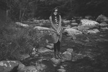 Woman wearing sunglasses standing on a rock in a stream.