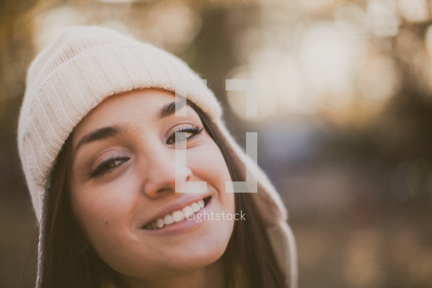 A young woman smiling in a white beanie