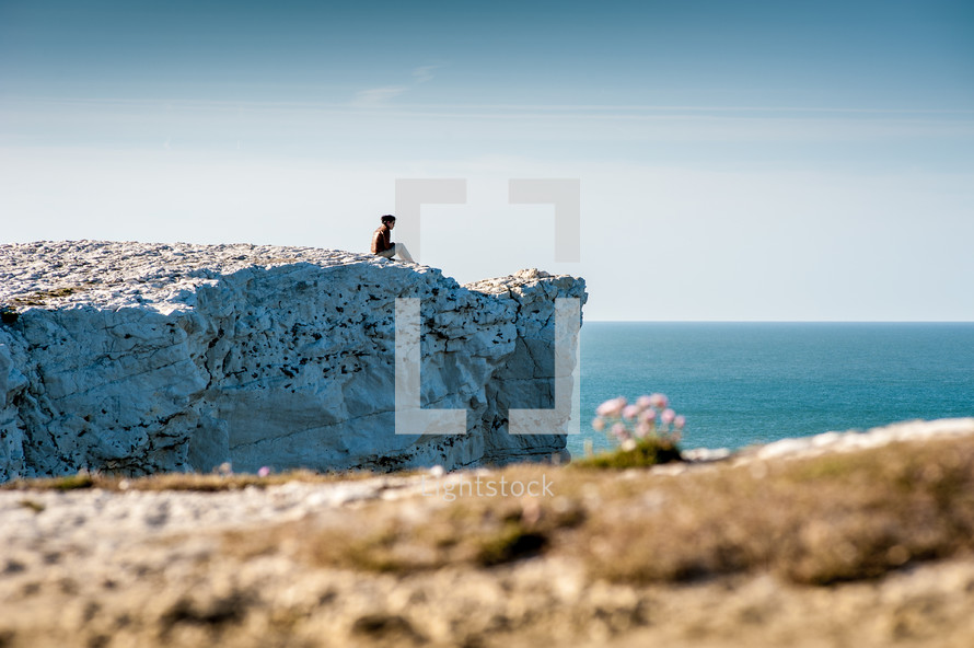 a woman sitting on the edge of a cliff over the ocean 