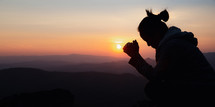 Silhouette of a woman praying at sunset