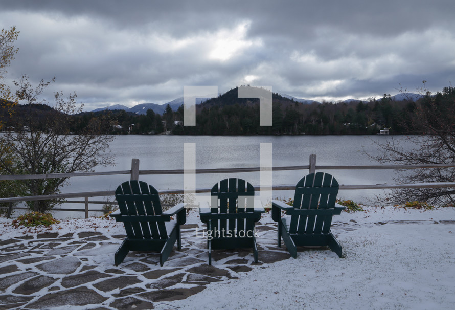 adirondack chairs in the snow overlooking a lake 