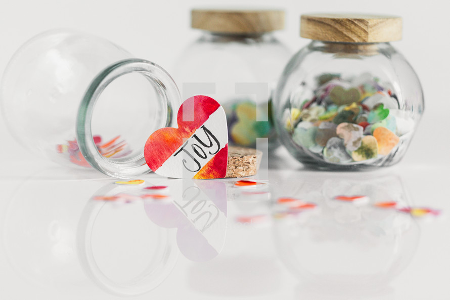 Jars of paper hearts on a white background with one lettered JOY in front.