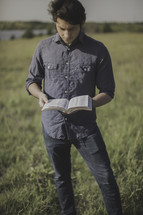 a man standing in a field reading a Bible 