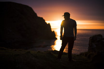 silhouette of a man standing on a shore at sunset 