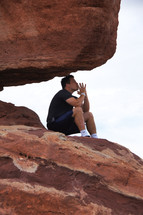 Man praying and in deep thought on a red rock at the top of a mountain