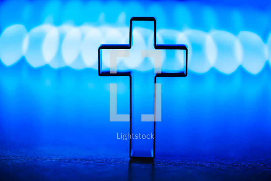 Silhouette of christian cross on soft bokeh lights background. Copy space. 