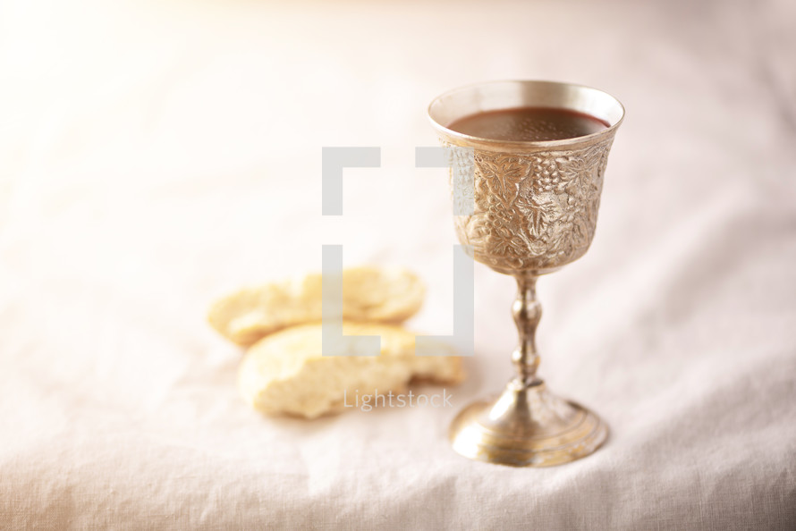 Unleavened bread, chalice of wine, silver kiddush wine cup on canva background. Communion still life. Christian communion concept for reminder of Jesus sacrifice. Easter passover