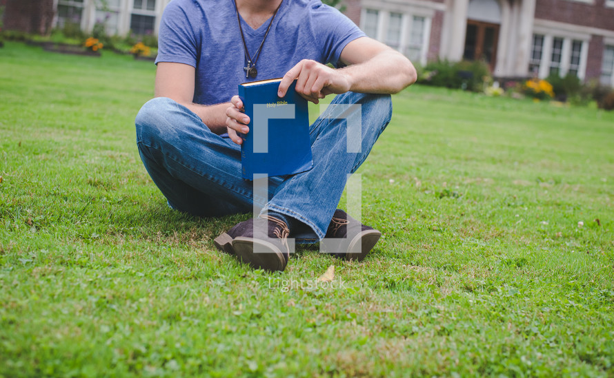 A man holds a Bible on a lawn outside an apartment complex