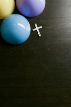 Silver cross on wooden table with colorful plastic Easter eggs.